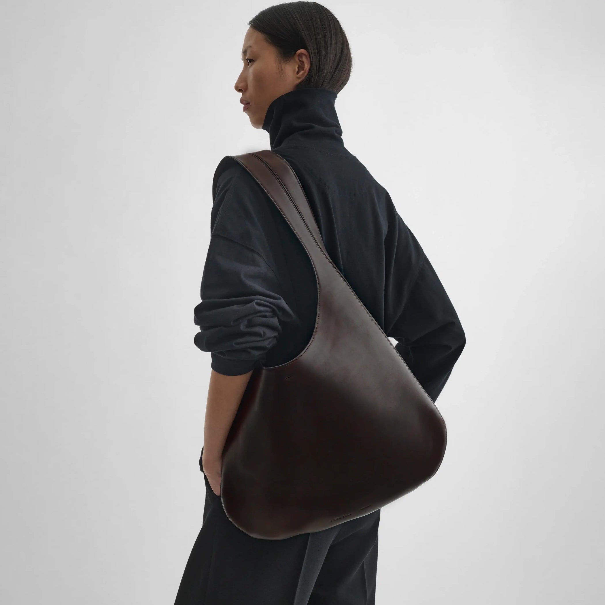 Model holding bean sling bag in chocolate brown leather. 