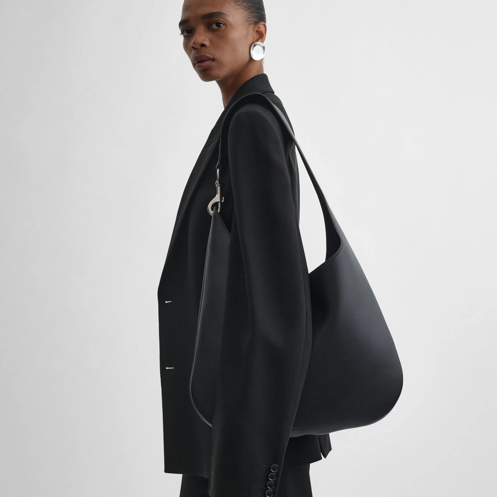 Model holding bean sling bag in black leather. 