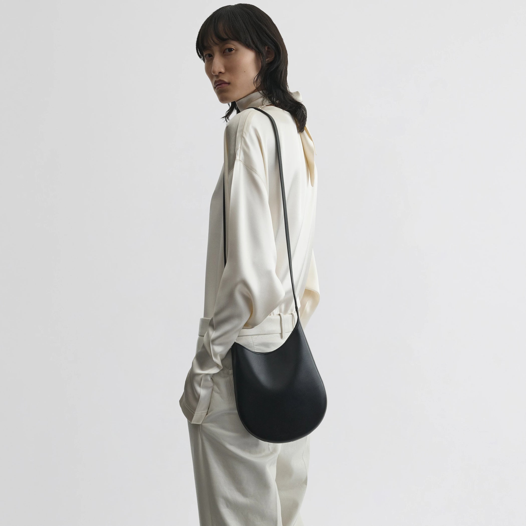 Side view of model wearing mini bean sling in black leather.
