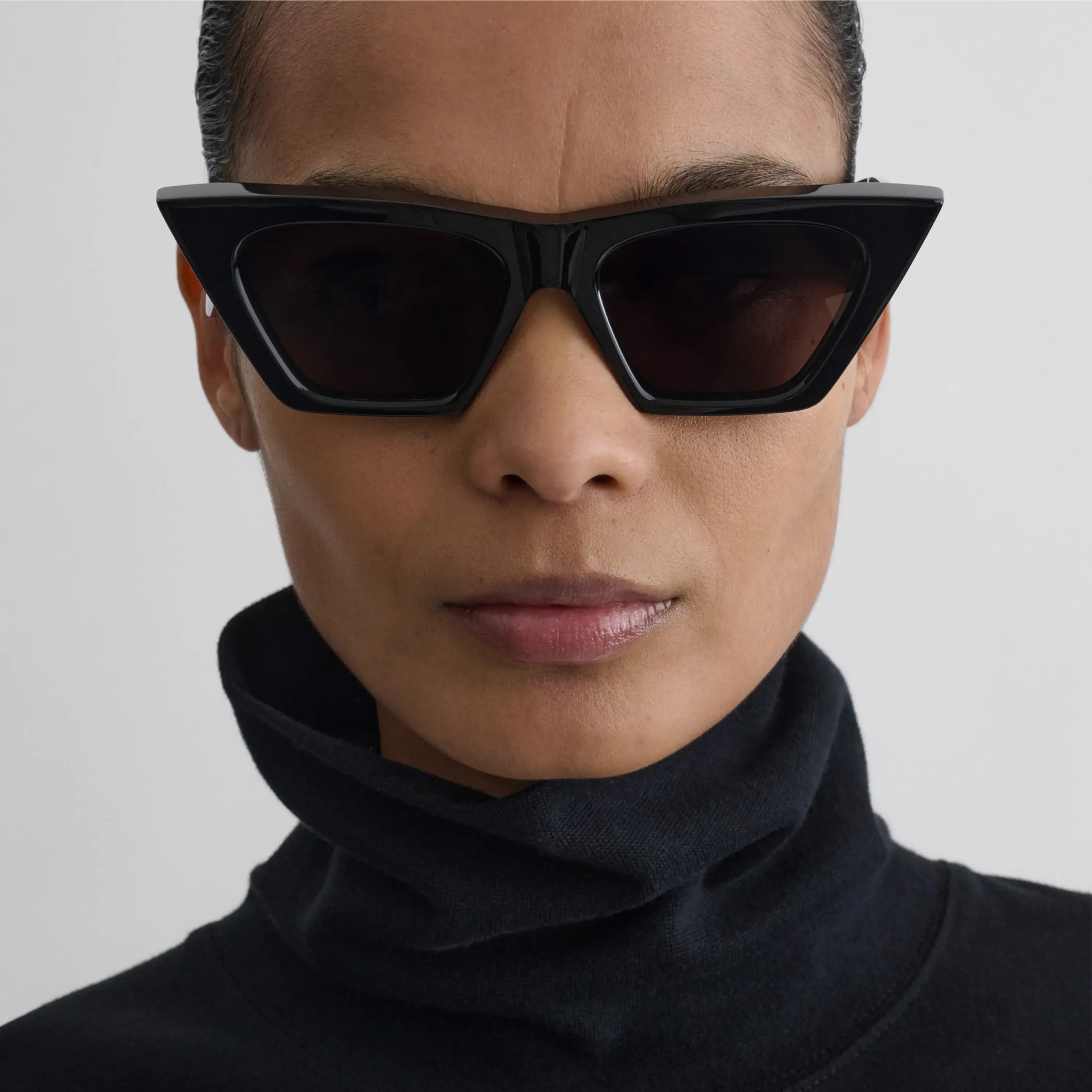 Front view of model wearing peak sunglasses in black acetate.
