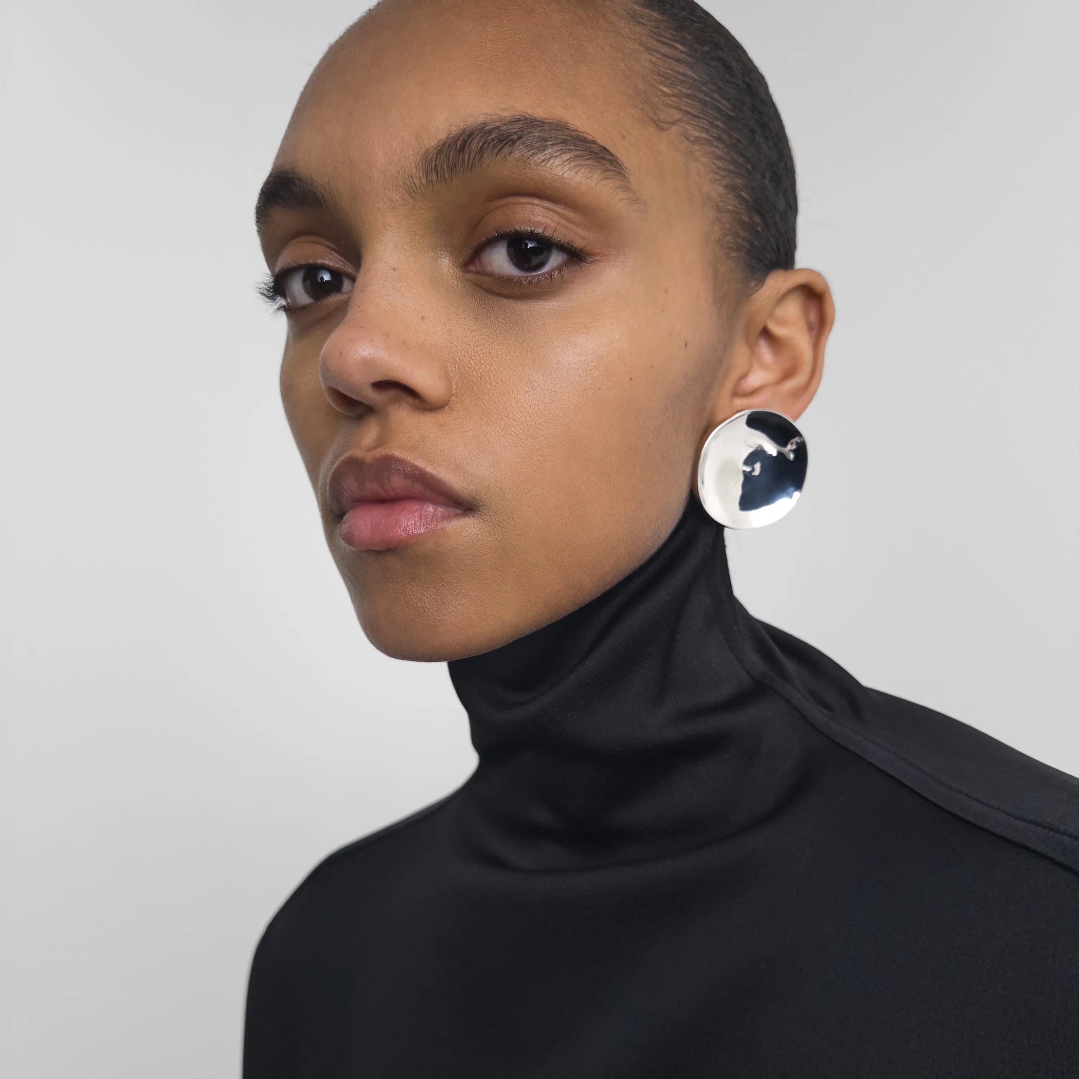 Model wearing medallion earrings in silver. 