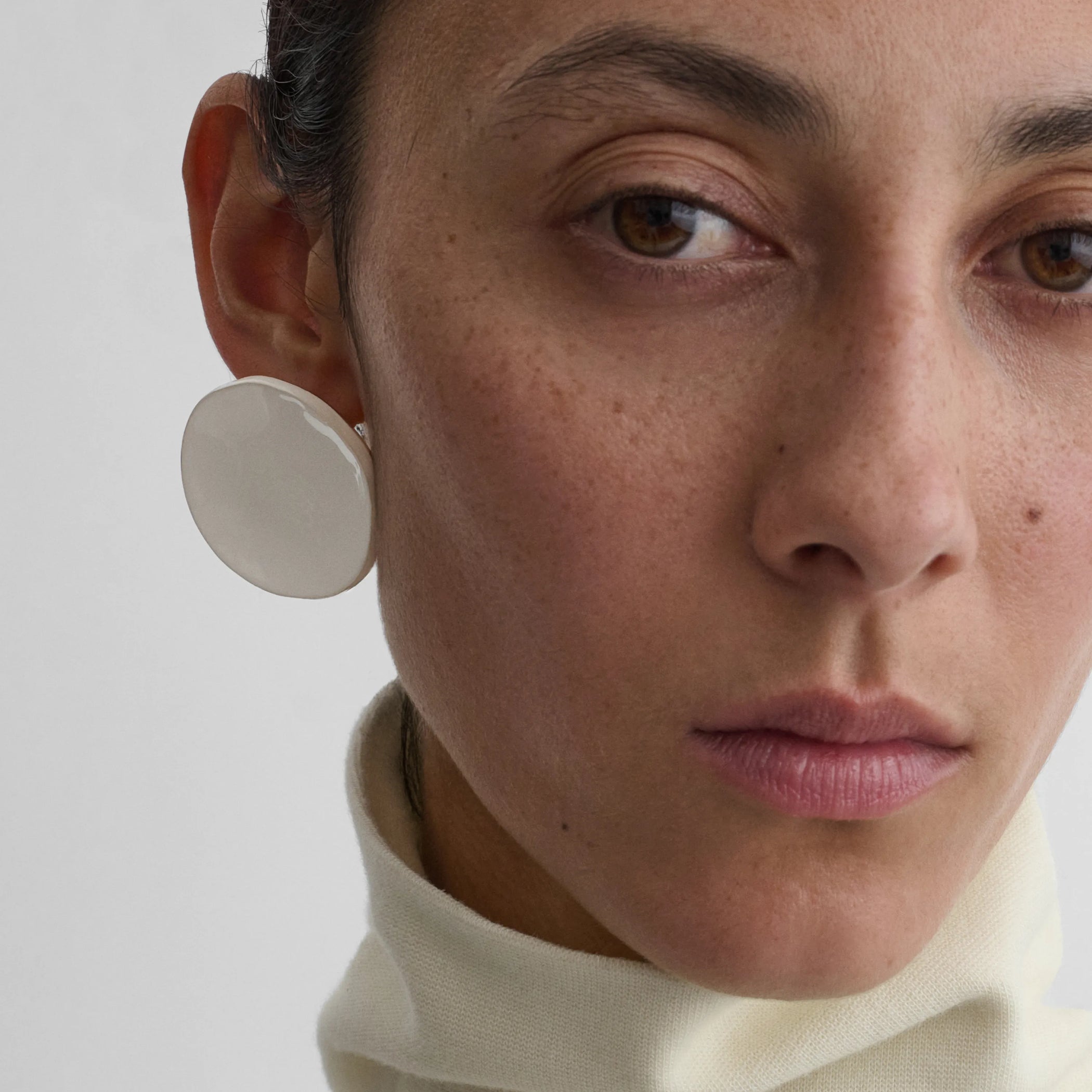 Front view of model wearing the medallion earrings in white 