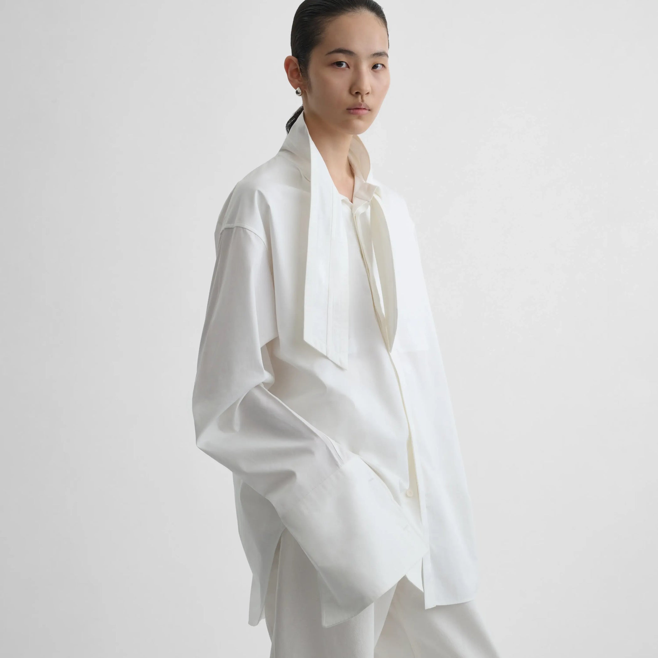 Side view of model wearing tie neck shirt in white