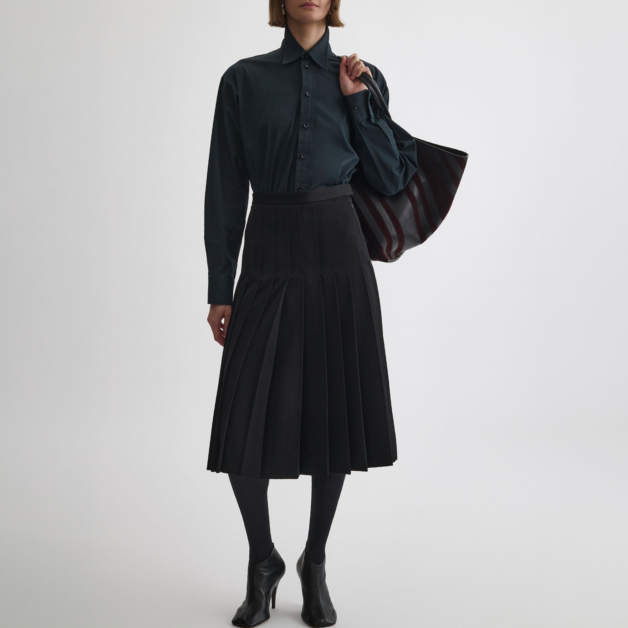 Front view of model wearing UNIFORM PLEATED SKIRT in black wool blend
