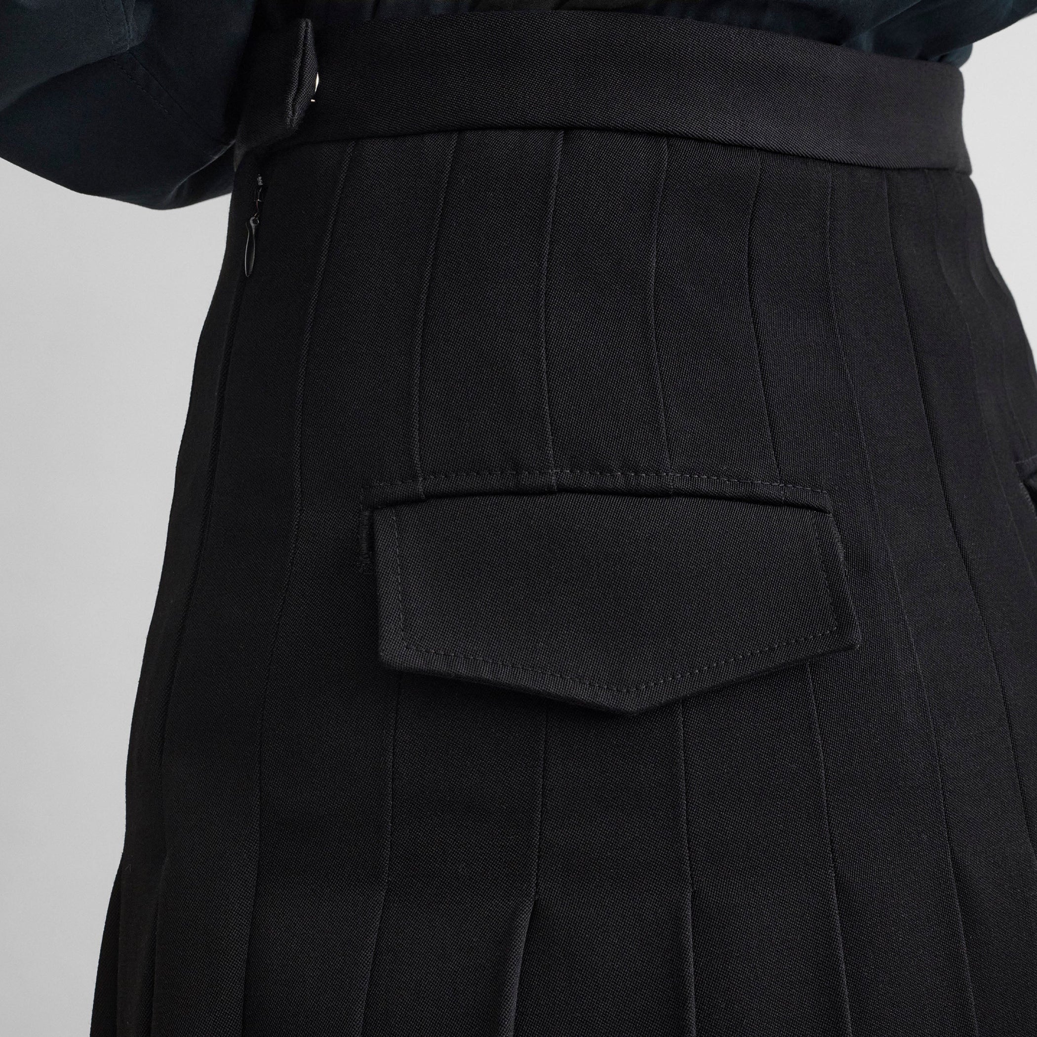 Close up detail view of model wearing UNIFORM PLEATED SKIRT in black wool blend