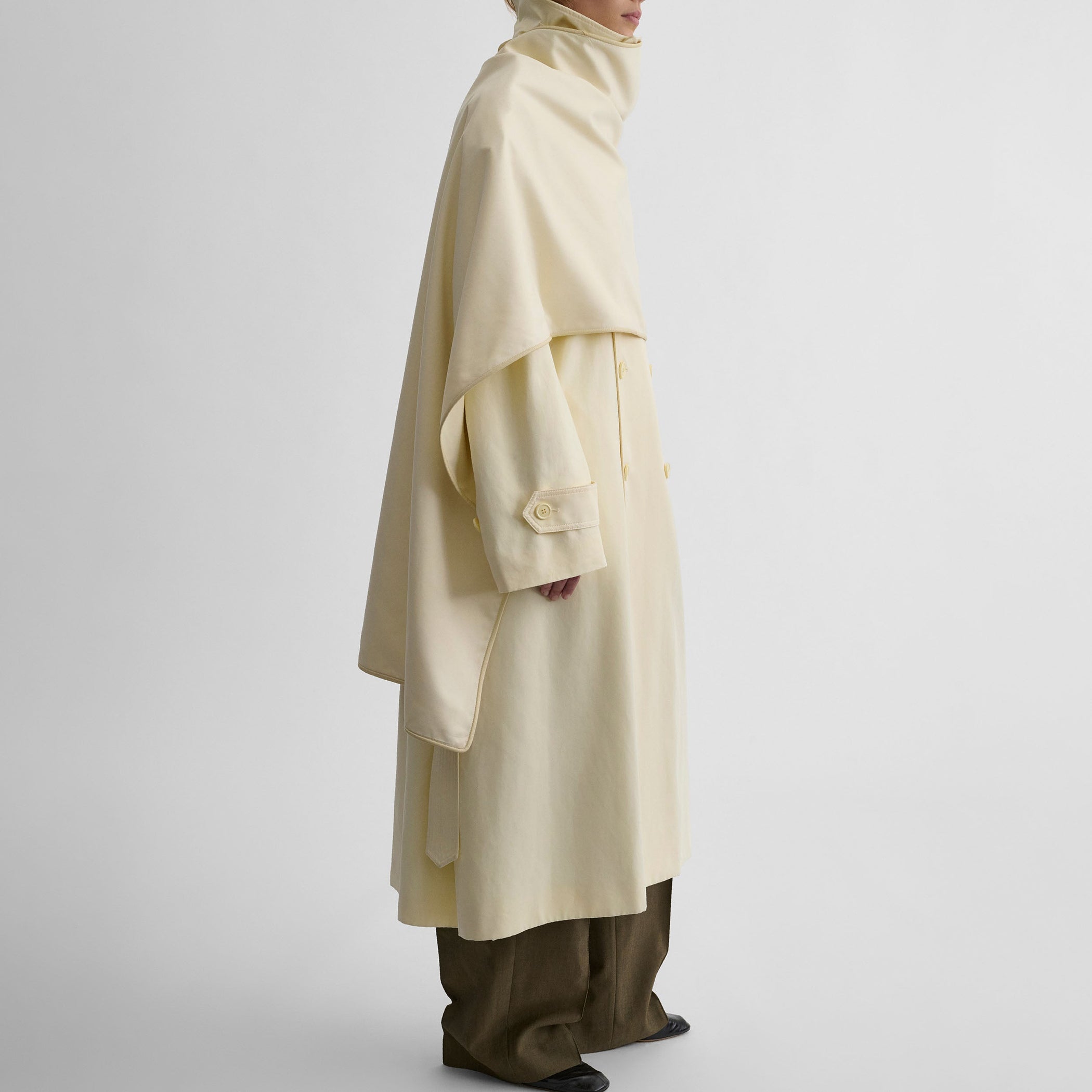 Side view of model wearing TRENCH COAT WITH ATTACHABLE SCARF in cream technical polyester