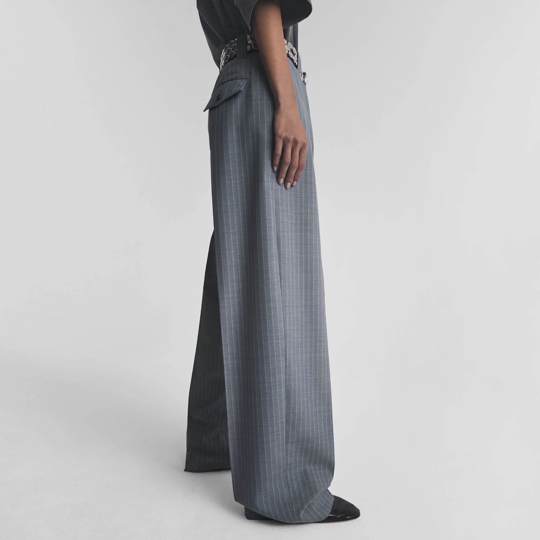 Side view of model wearing OVERSIZED TROUSERS in steel grey pinstripe wool