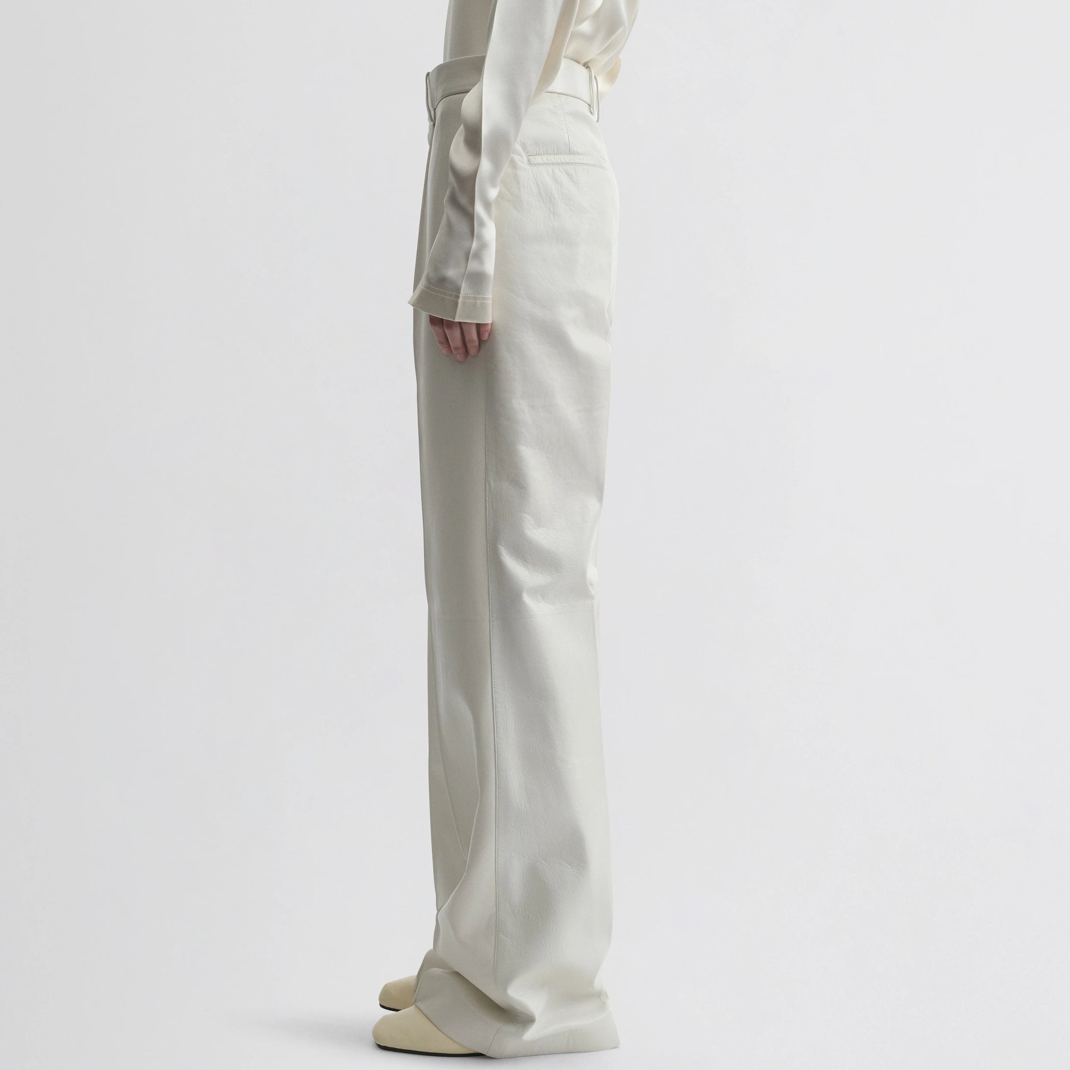 Side view of model wearing boyish trousers in white leather.