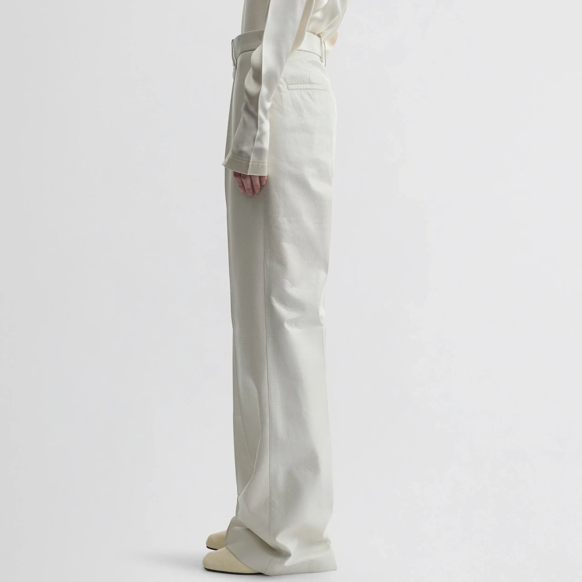 Side view of model wearing boyish trousers in white leather.