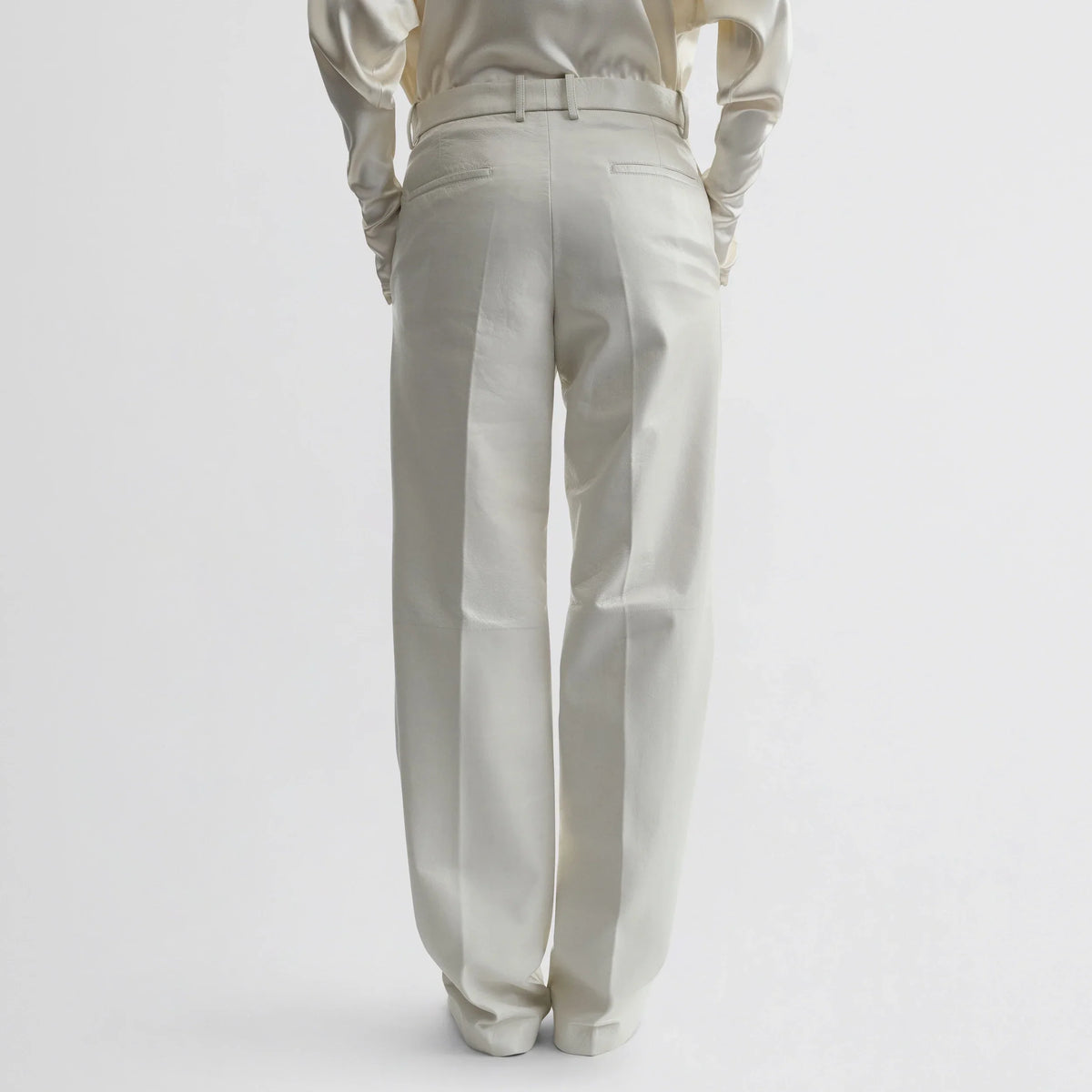 Back view of model wearing boyish trousers in white leather.