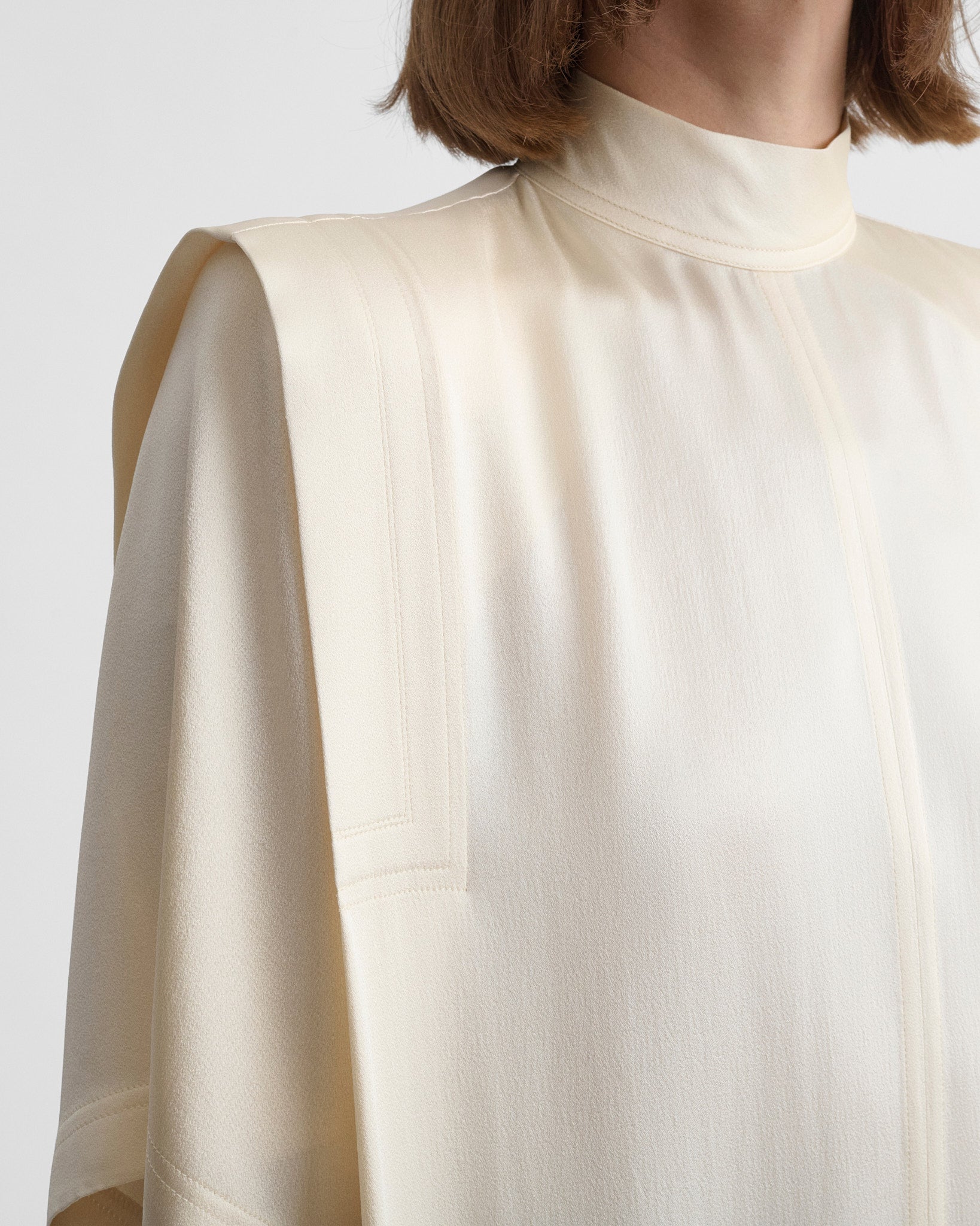 Angled back view of model wearing folded shoulder dress in vanilla satin back crepe
