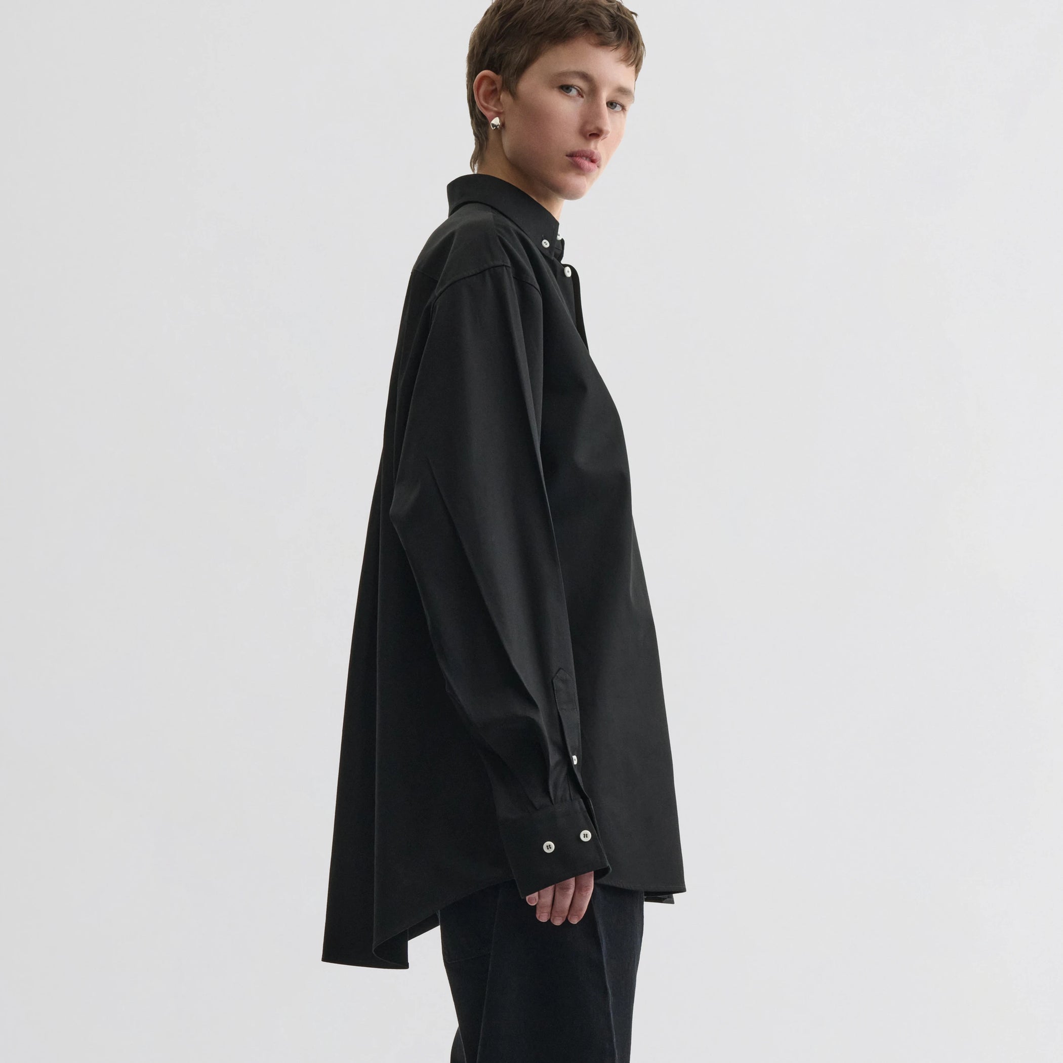 Side view of model wearing button collar shirt in black cotton.