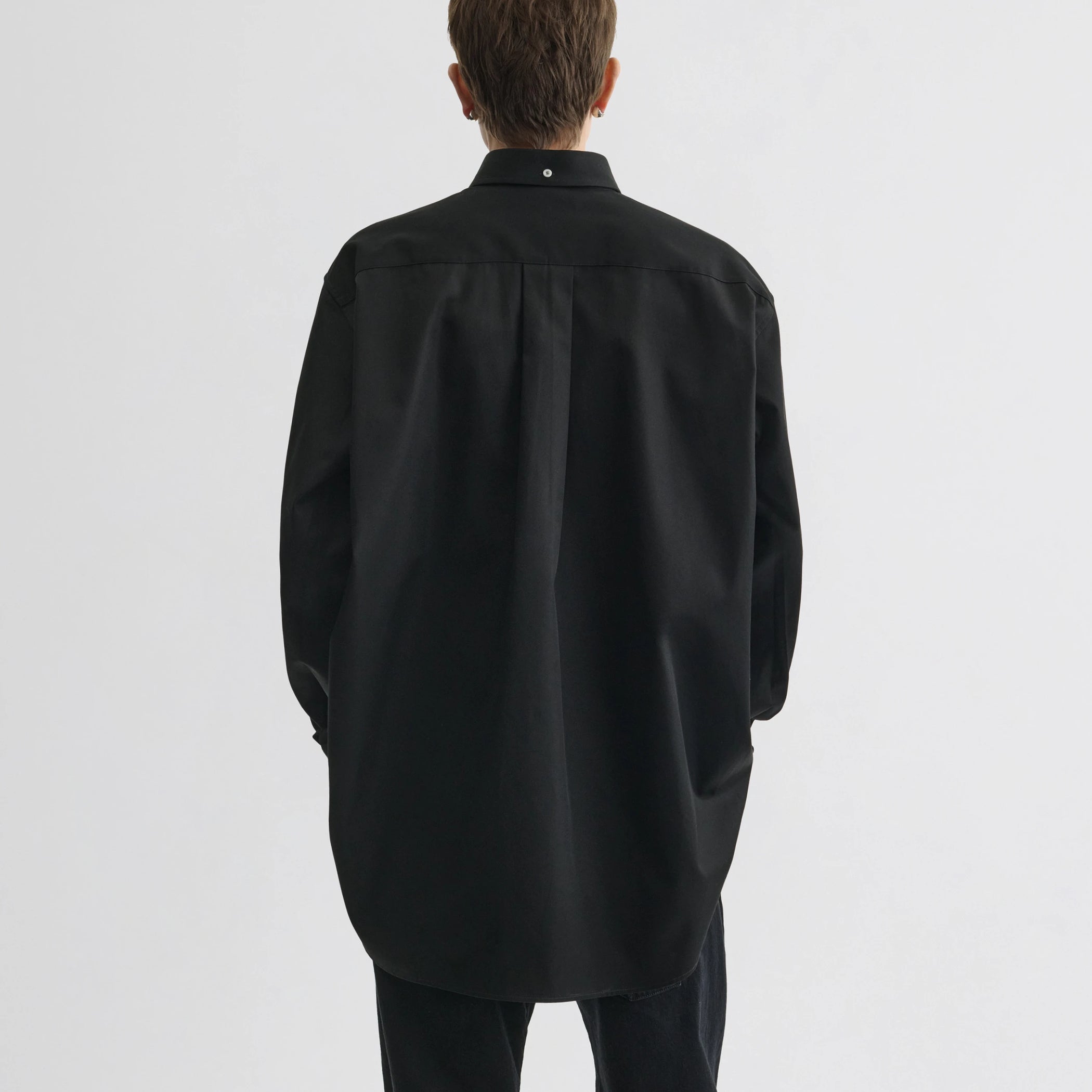 Back view of model wearing button collar shirt in black cotton.