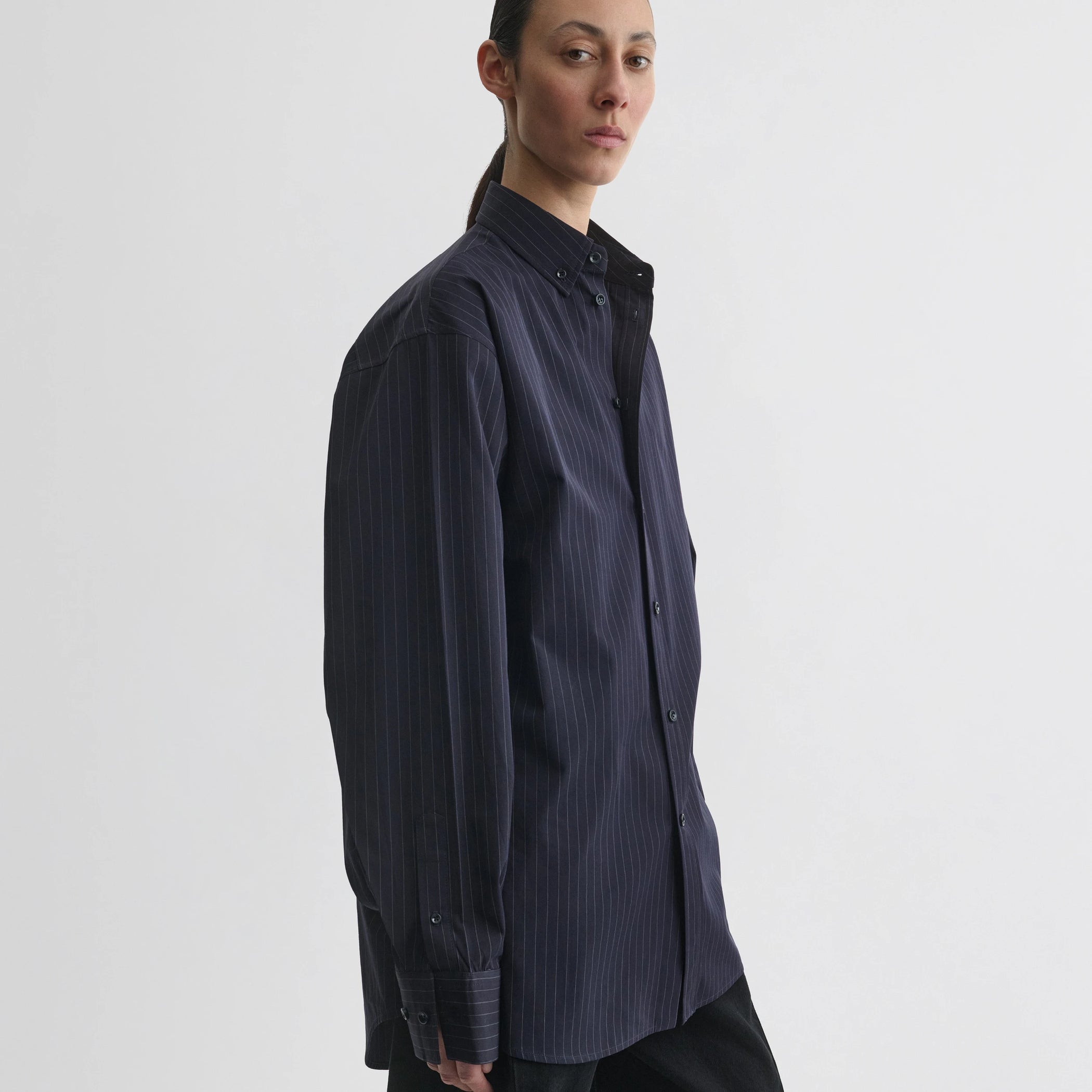 Side view of model wearing button collar shirt in midnight pinstripe cotton.