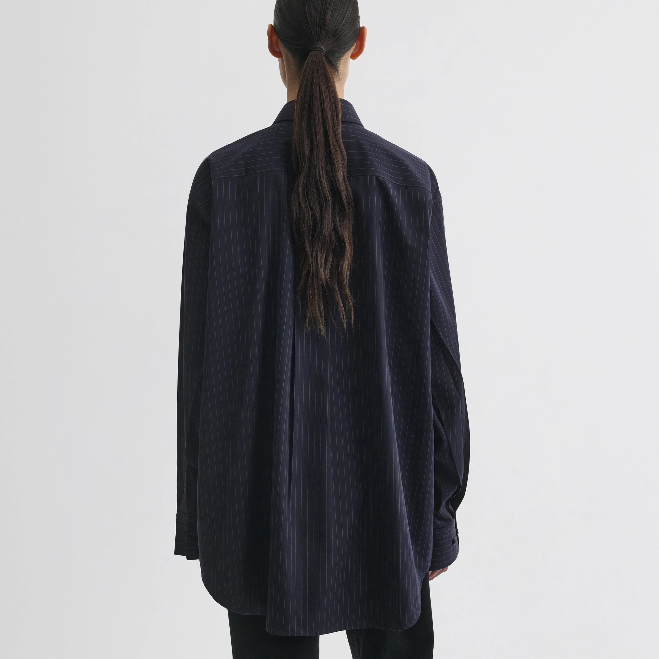 Back view of model wearing button collar shirt in midnight pinstripe cotton.