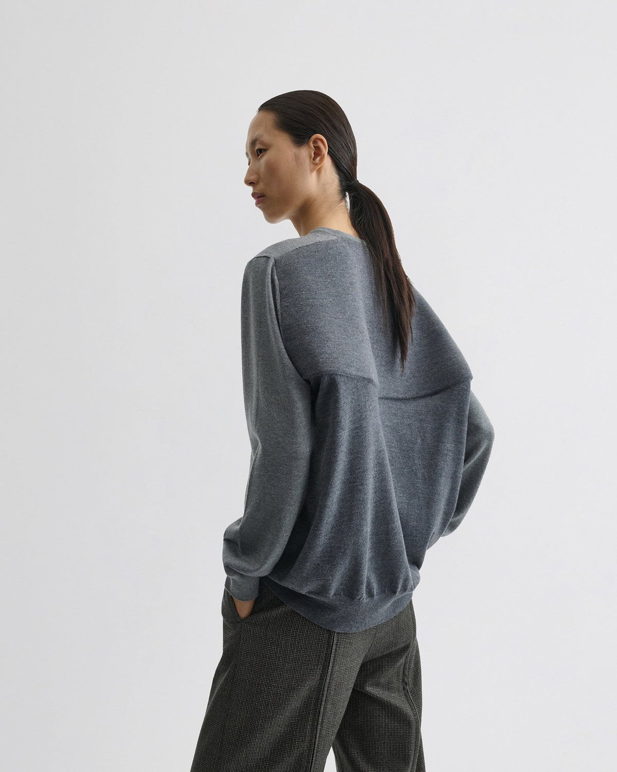Angled view of model wearing BACKED V NECK SWEATER in light grey wool