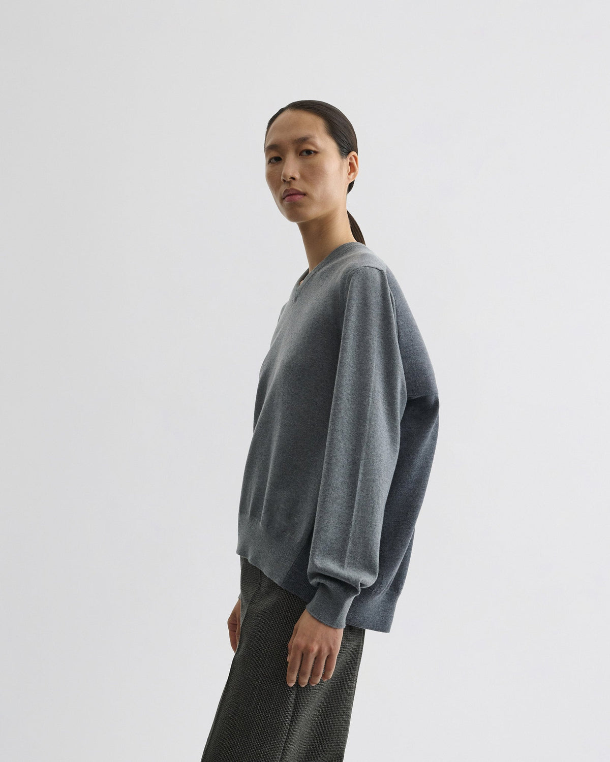 Side view of model wearing BACKED V NECK SWEATER in light grey wool