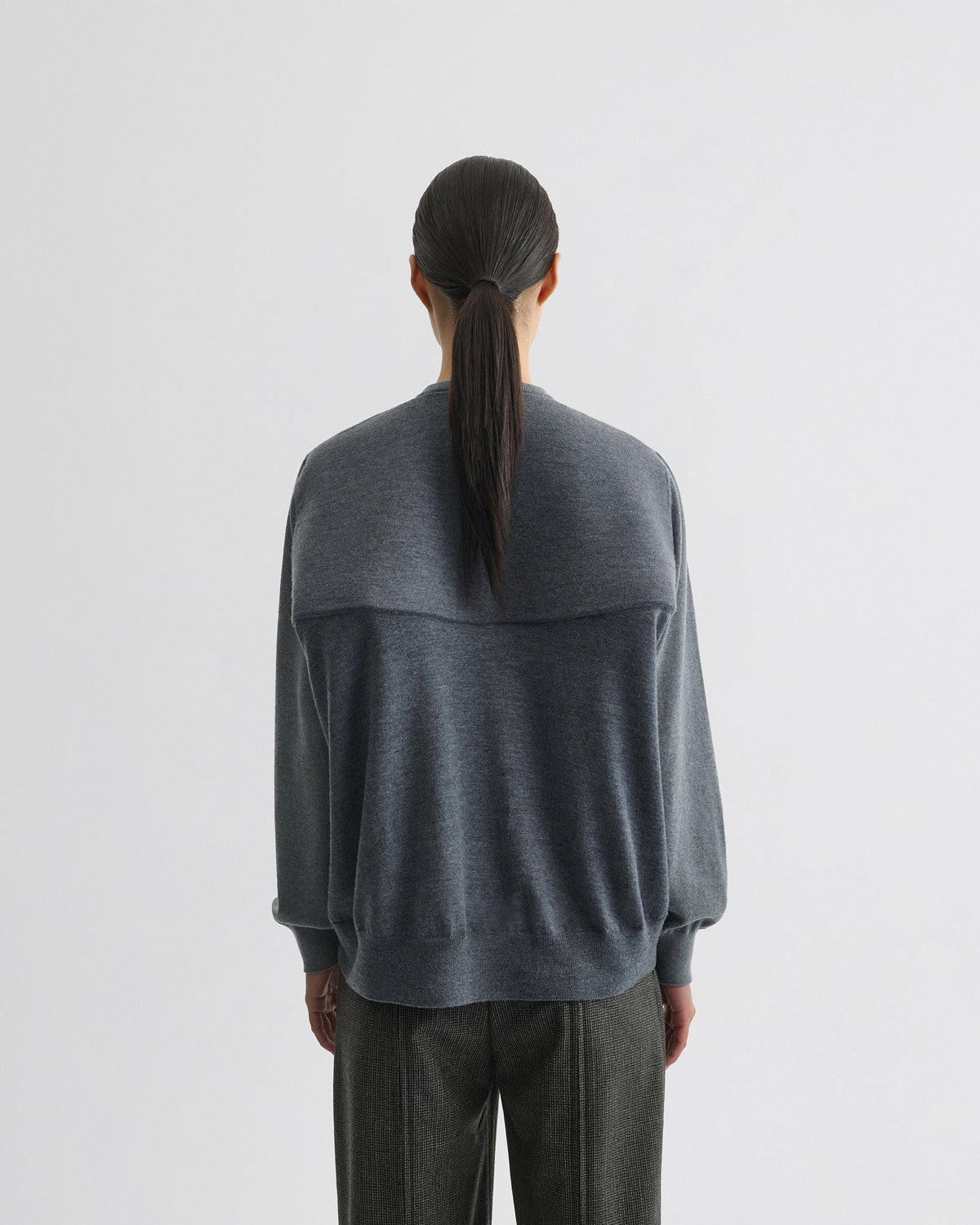 Back view of model wearing BACKED V NECK SWEATER in light grey wool