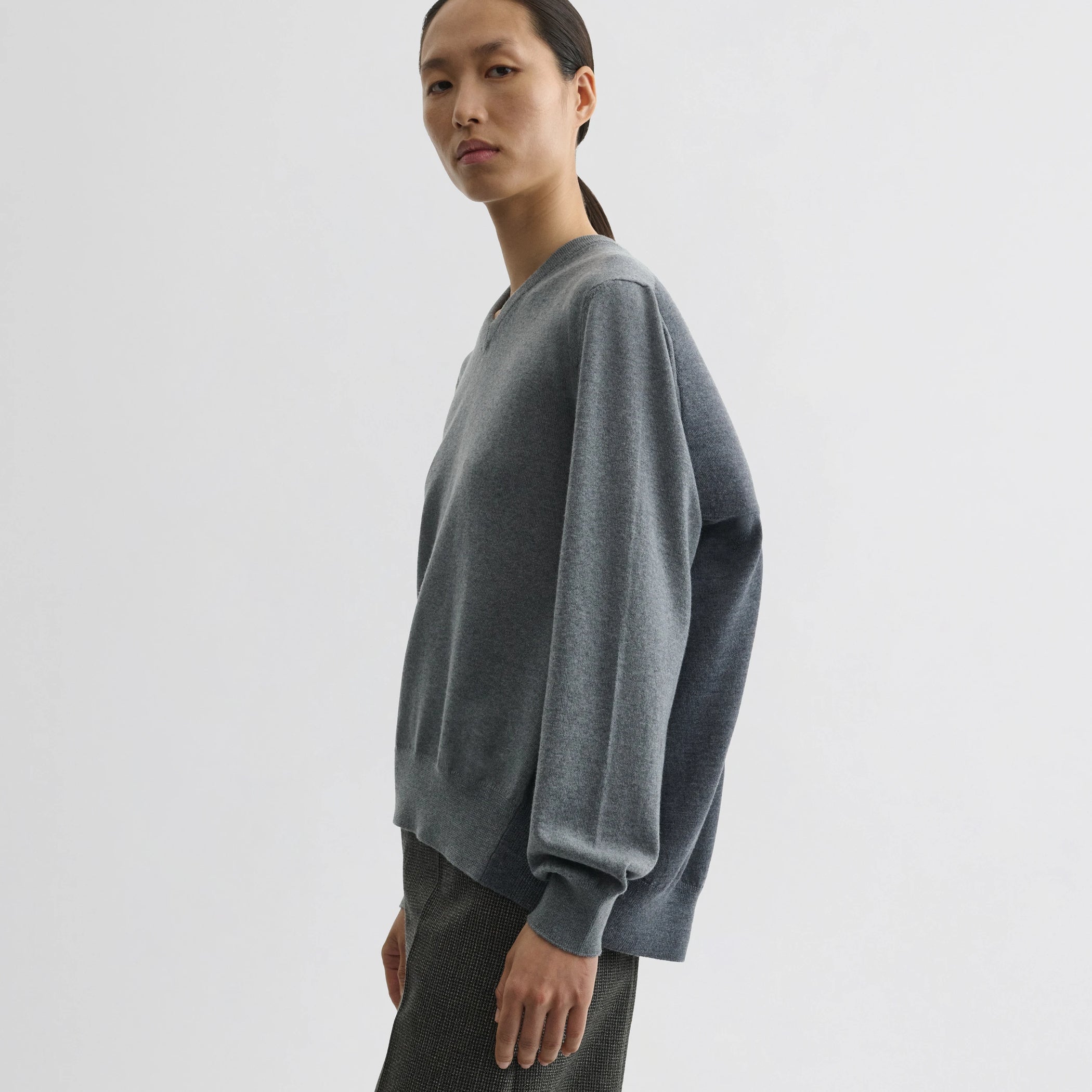 Side view of model wearing backed v-neck sweater in light grey wool.