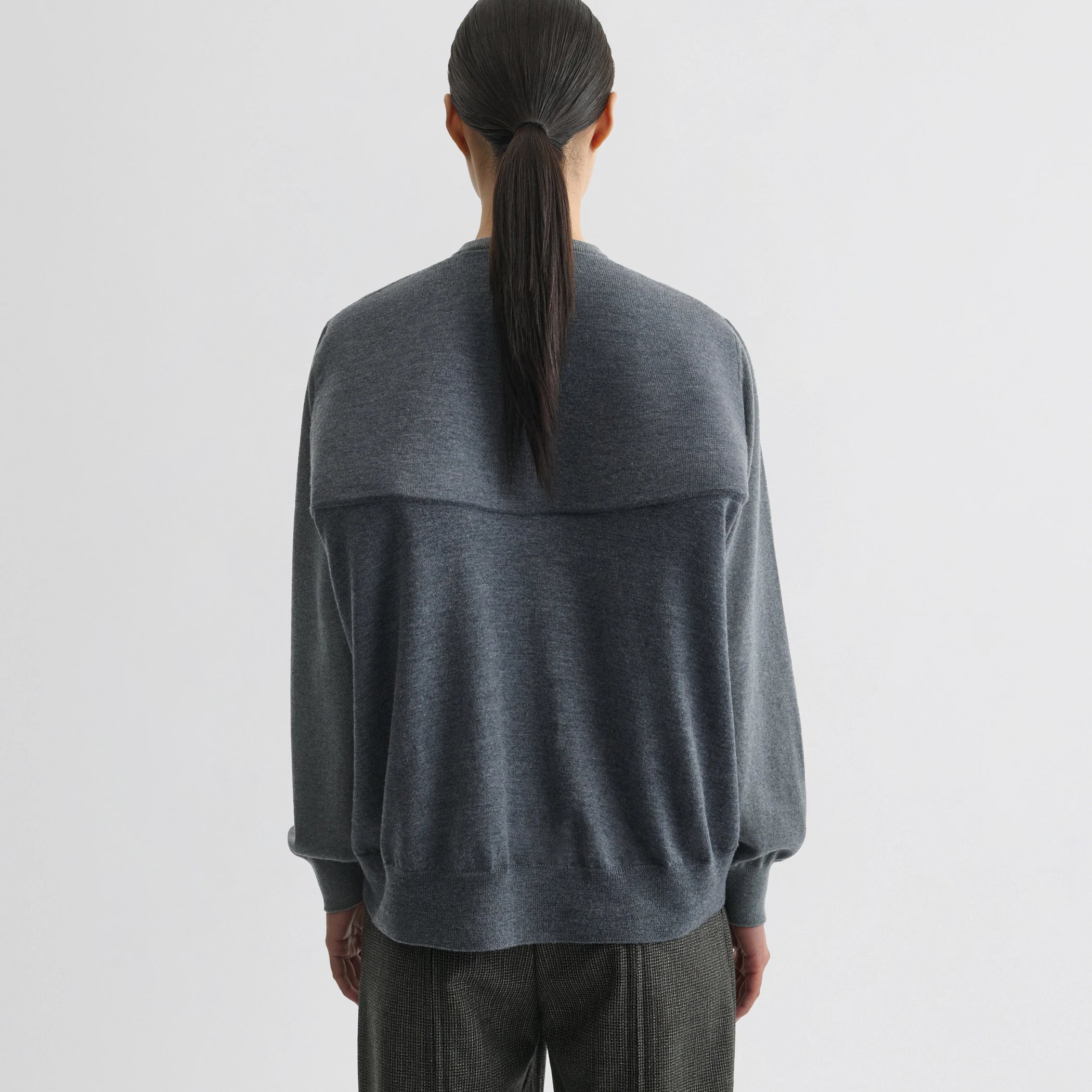 Back view of model wearing backed v-neck sweater in light grey wool.