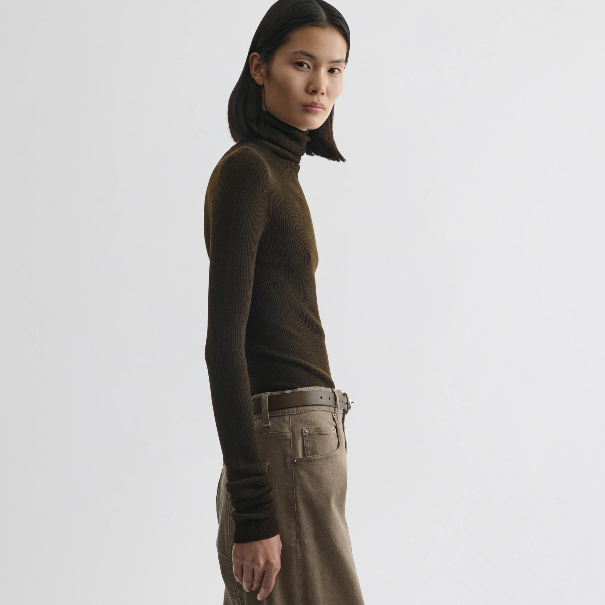 Side view of model wearing fine rib high neck top in dark khaki wool.