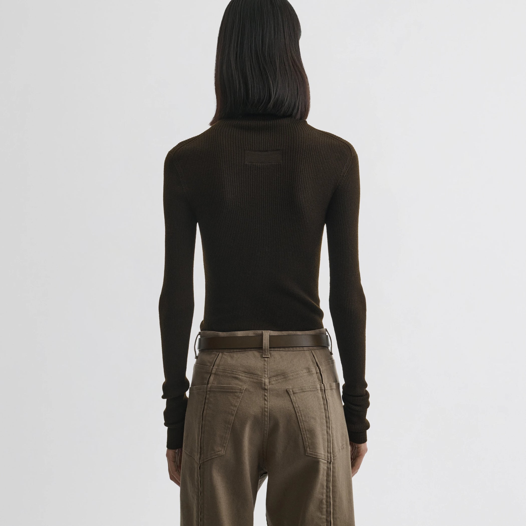 Back view of model wearing fine rib high neck top in dark khaki wool.