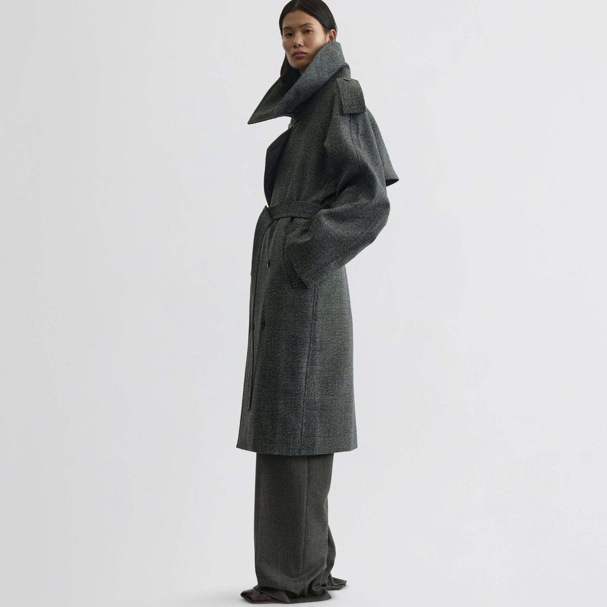 Side view of model wearing padded trench coat in salt and pepper wool.