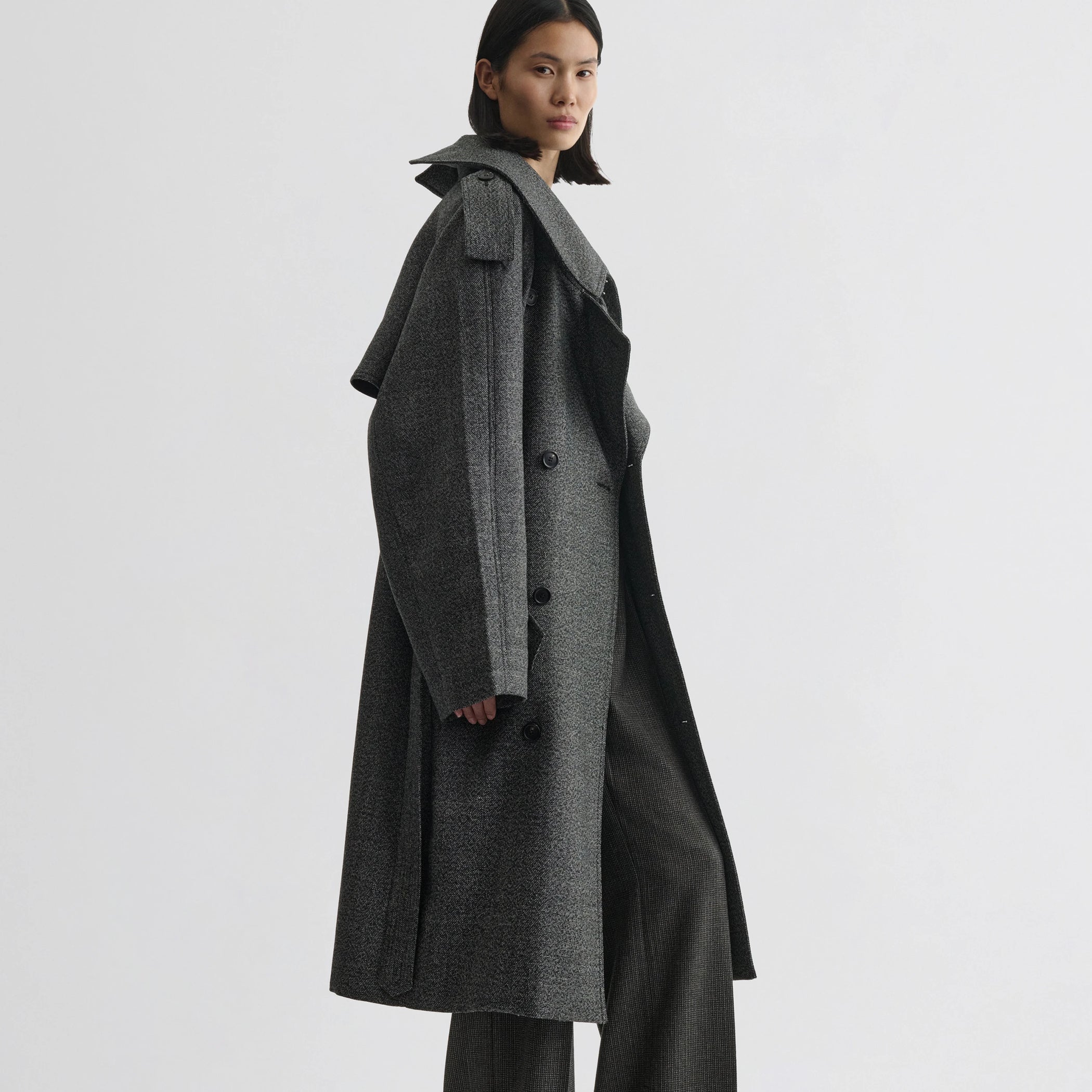 Side view of model wearing padded trench coat in salt and pepper wool.