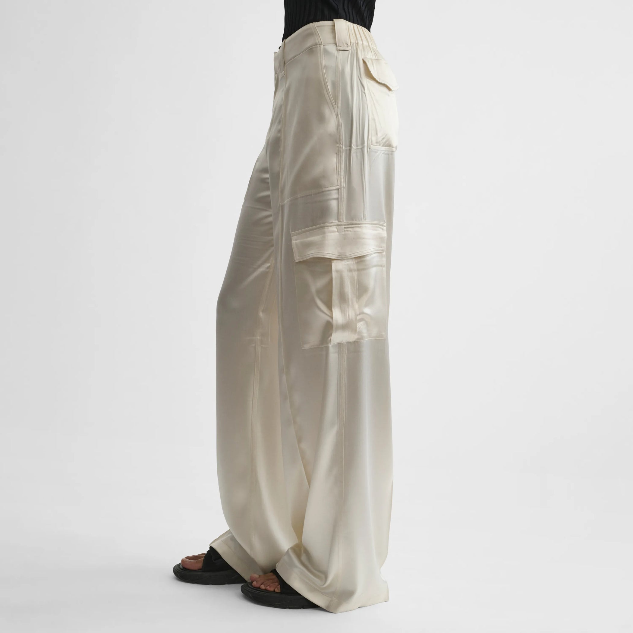 Side view of model wearing liquid cargo trousers in cream silk satin.