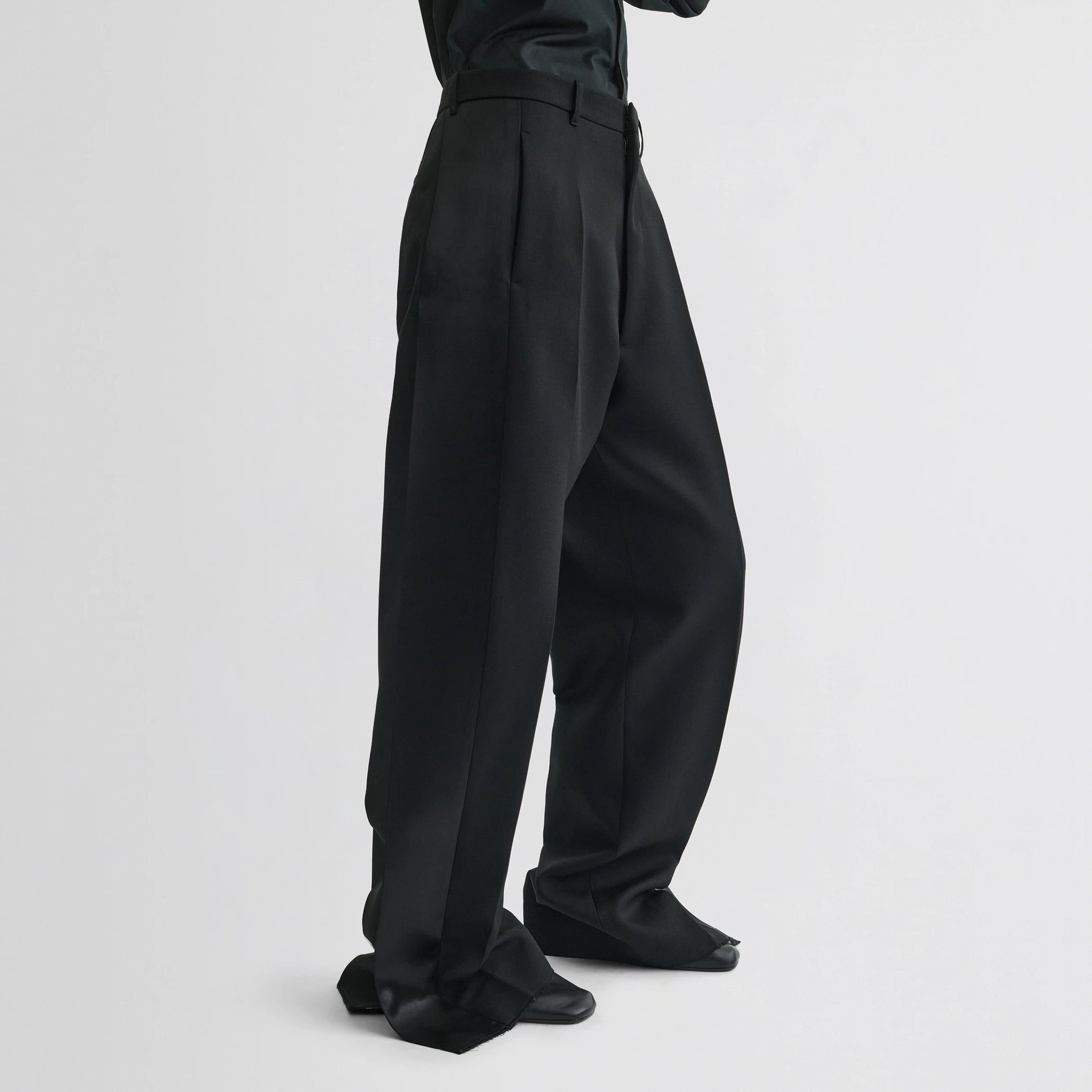 Side view of model wearing split tux trousers in black wool.