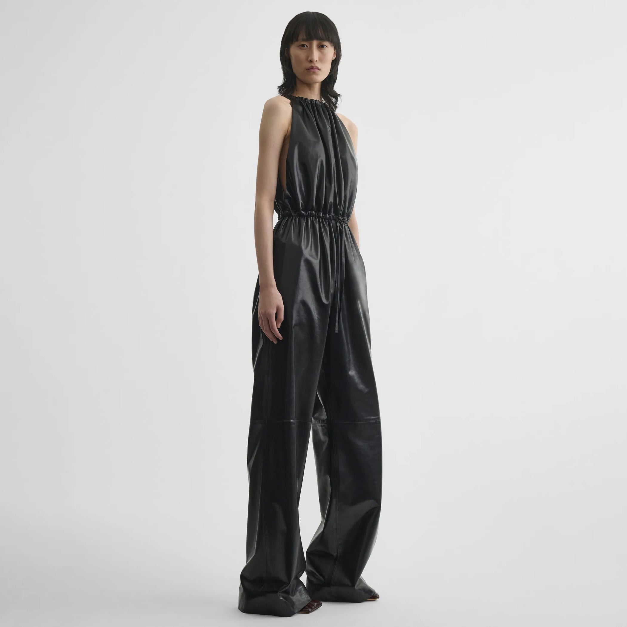 Side view of model wearing drawstring jumpsuit in black leather.