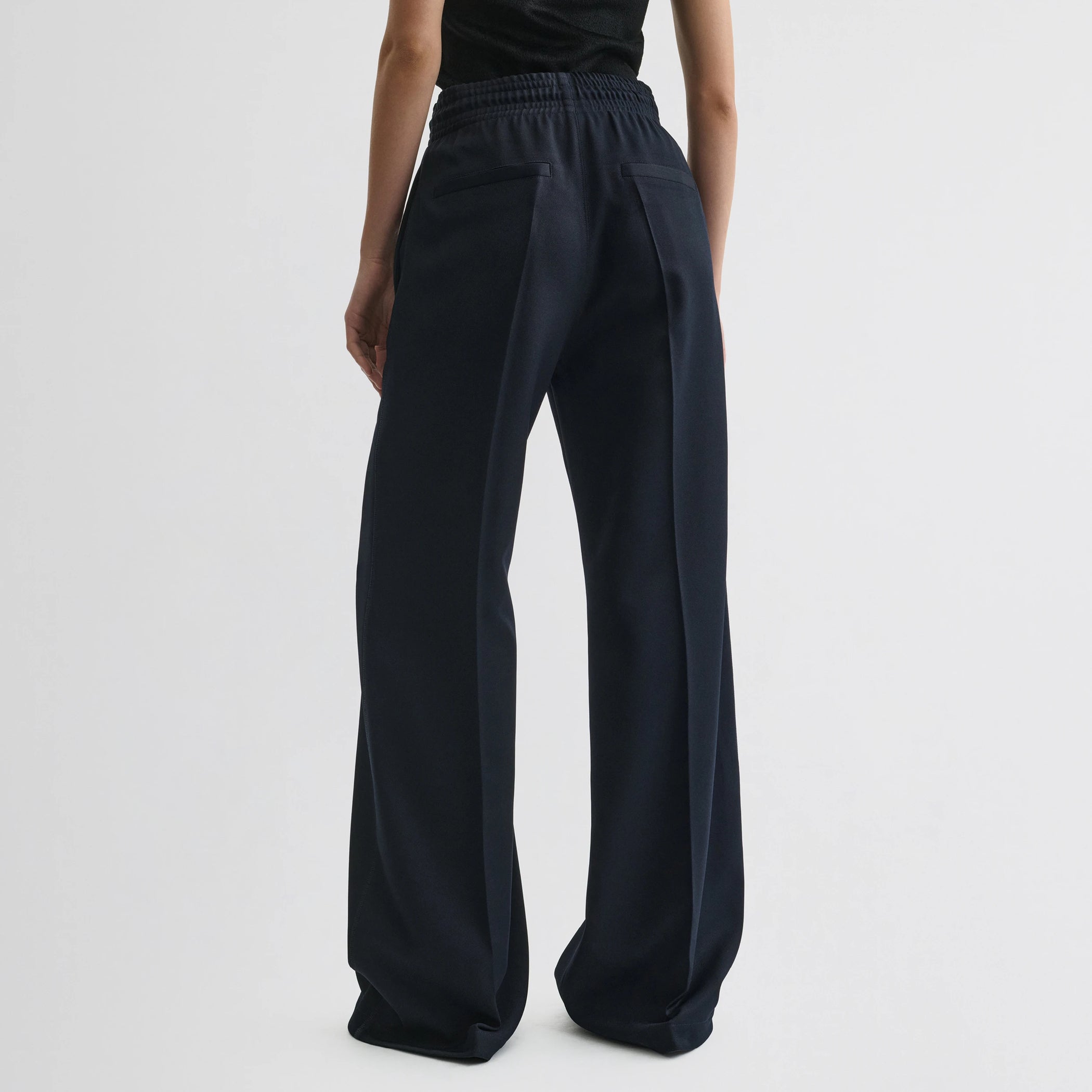 Back view of model wearing track trousers in navy polyester.