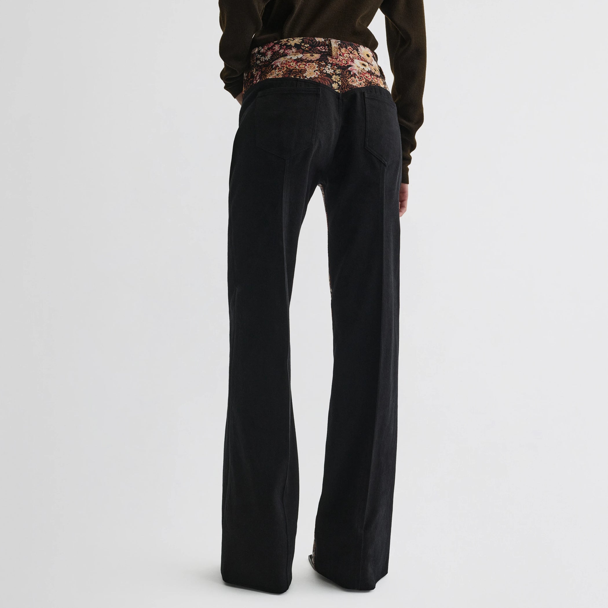 Back view of model wearing tapestry trousers in black cotton.