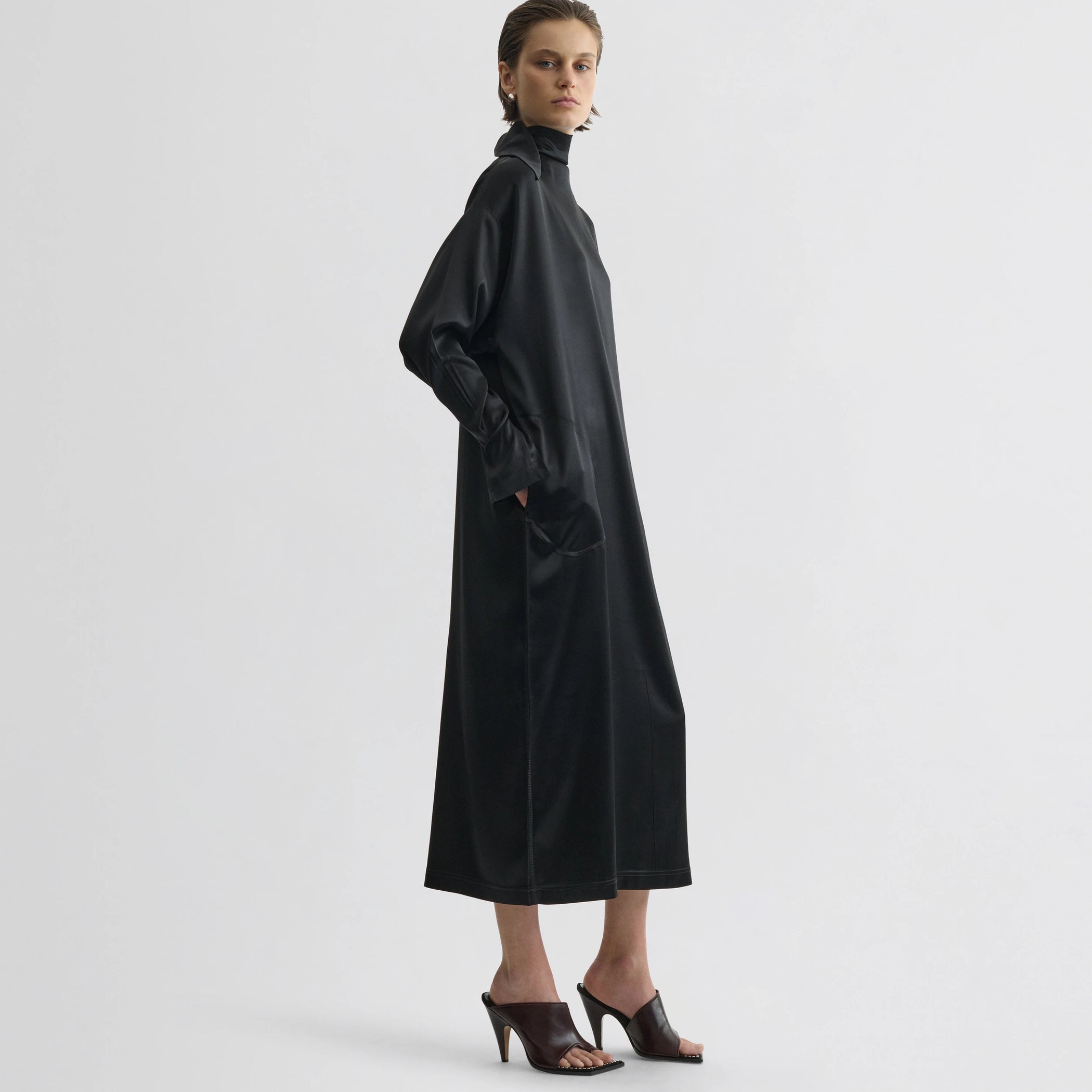 Side view of model wearing liquid high neck dress in black silk.