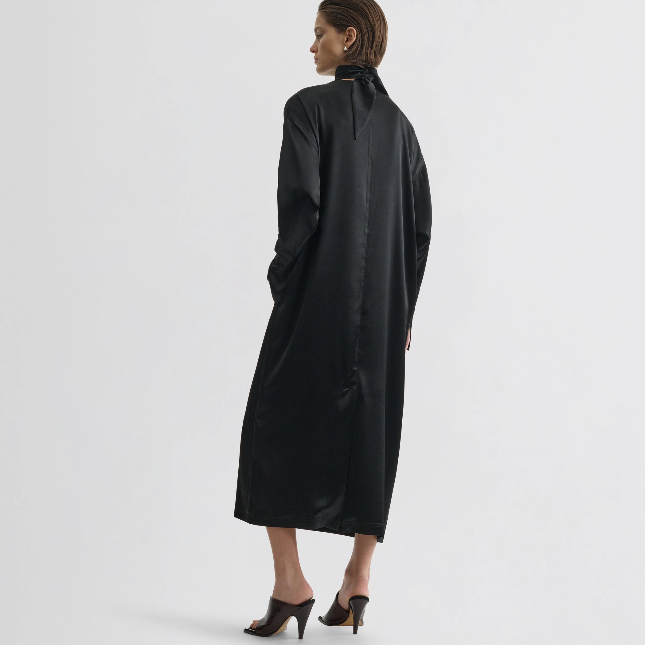 Back view of model wearing liquid high neck dress in black silk.