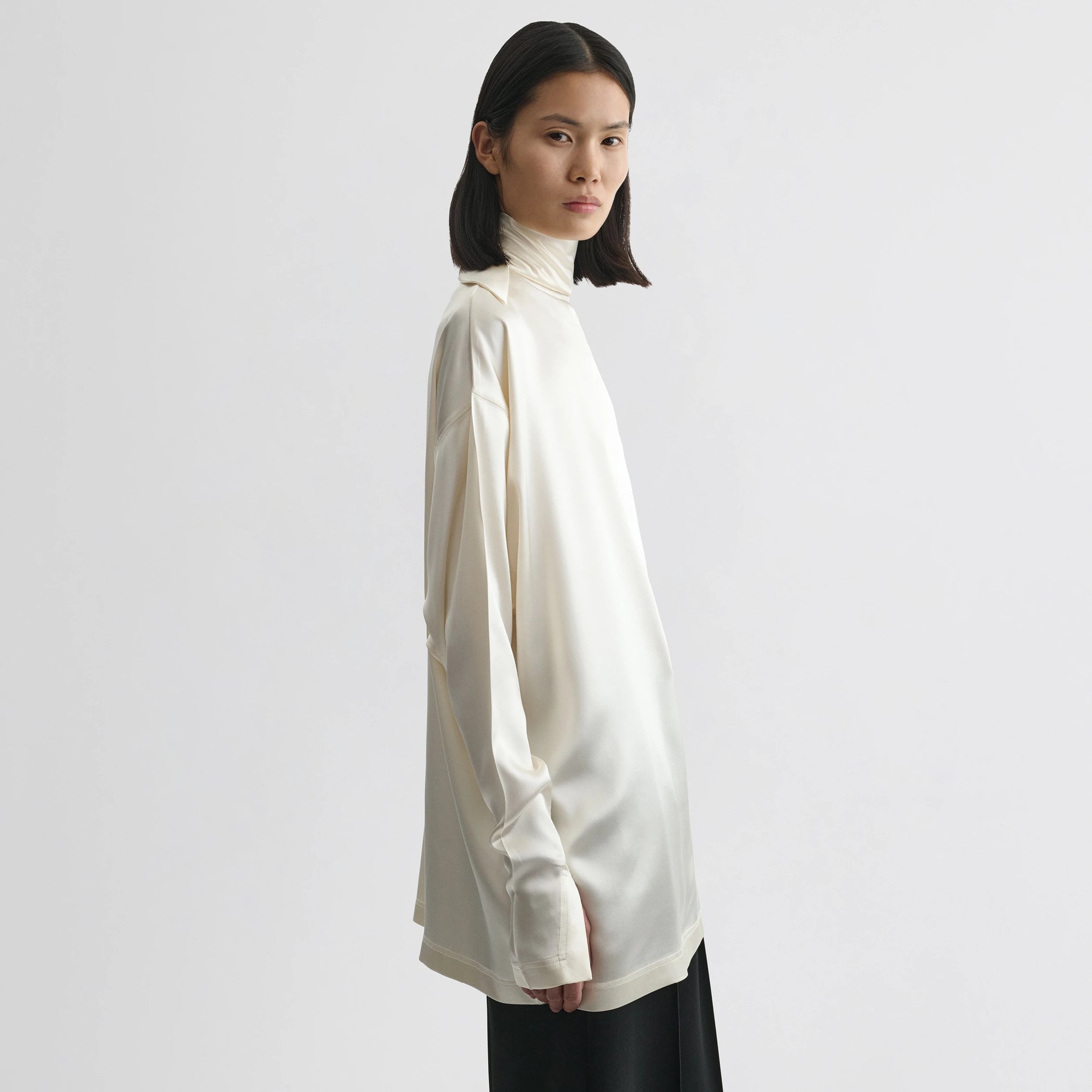 Side view of model wearing liquid knot collar top in cream silk.