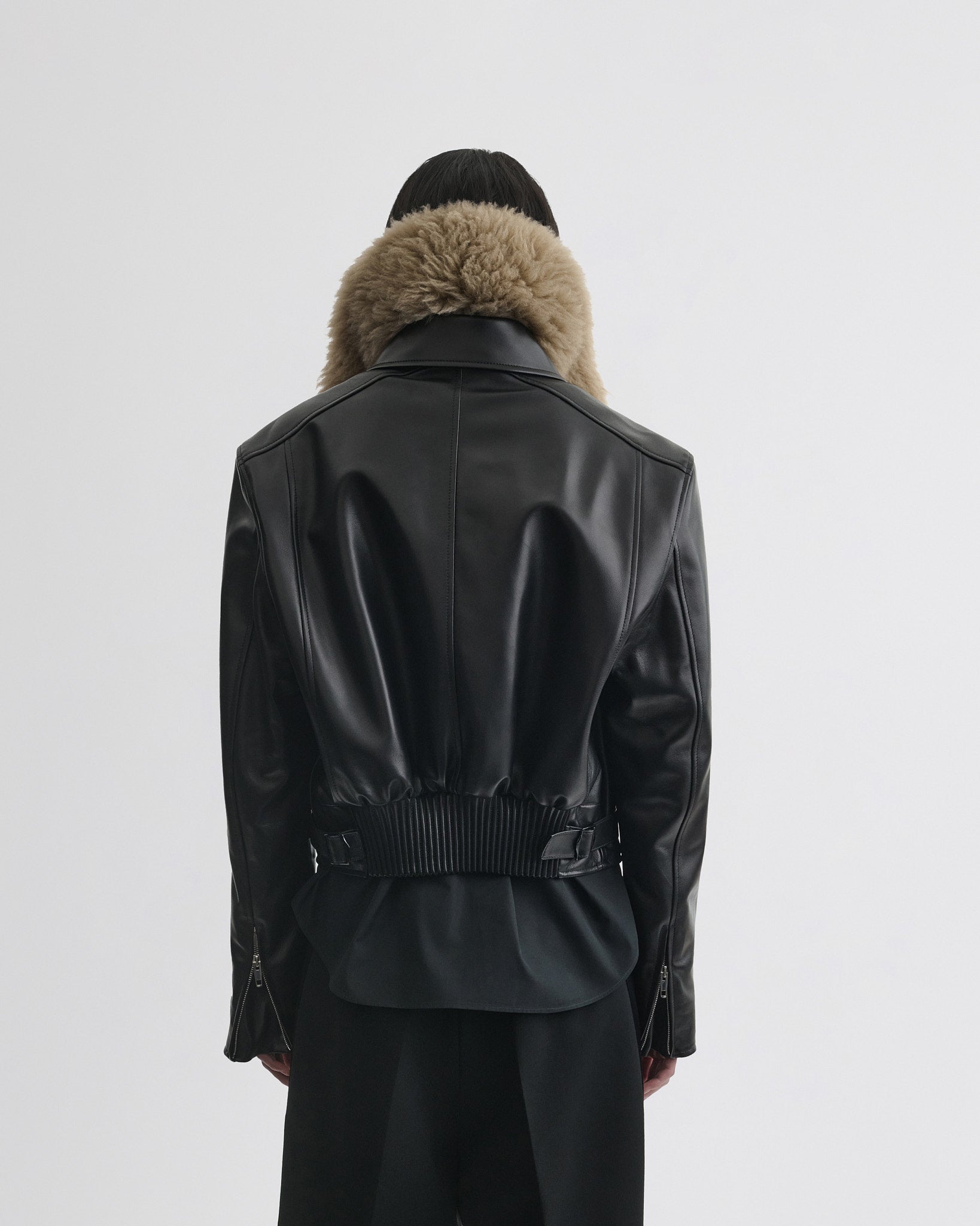 Back view of model wearing cropped aviator jacket in black leather.