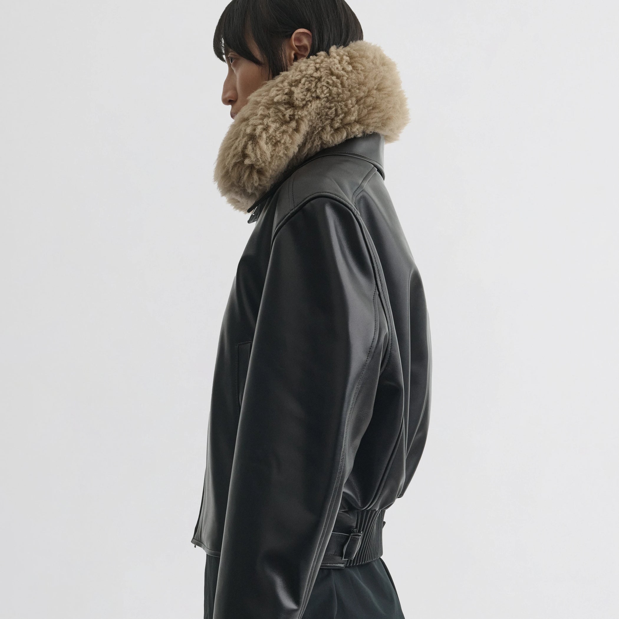 Side view of model wearing cropped aviator jacket in black leather.