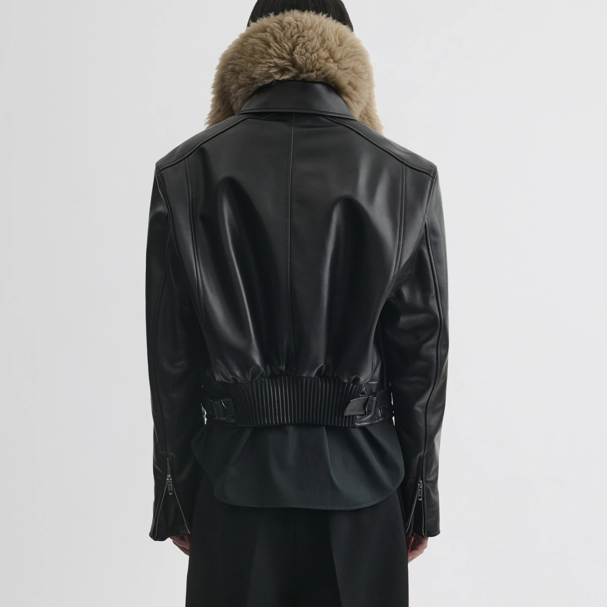 Back view of model wearing cropped aviator jacket in black leather.