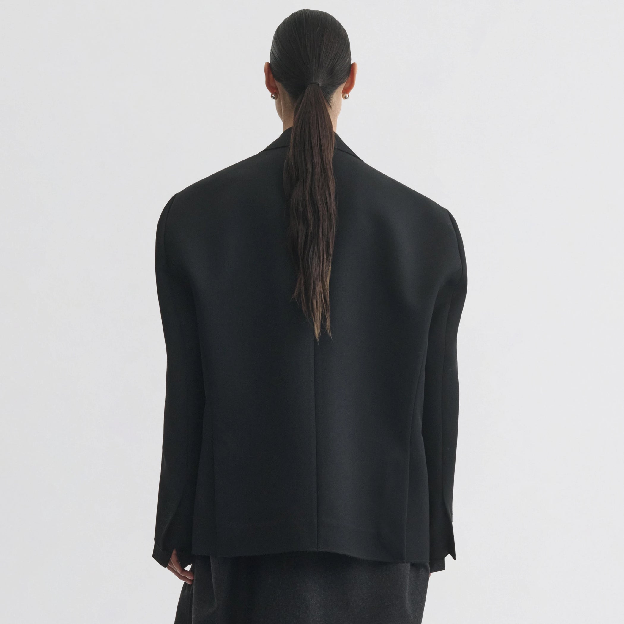 Back view of model wearing tuxedo jacket in black wool.