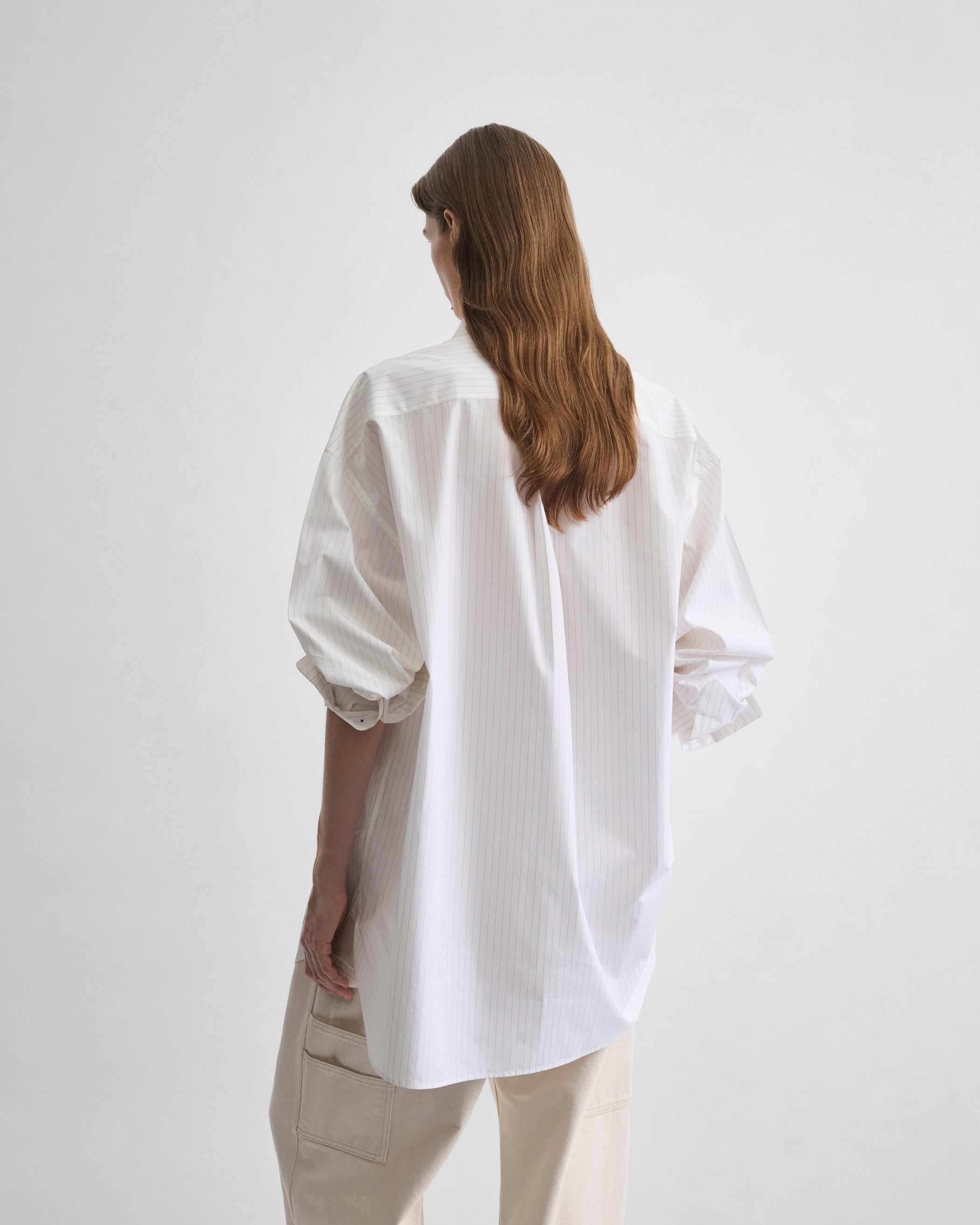 Angled back view of model wearing RELAXED TAILORED SHIRT in white/beige cotton