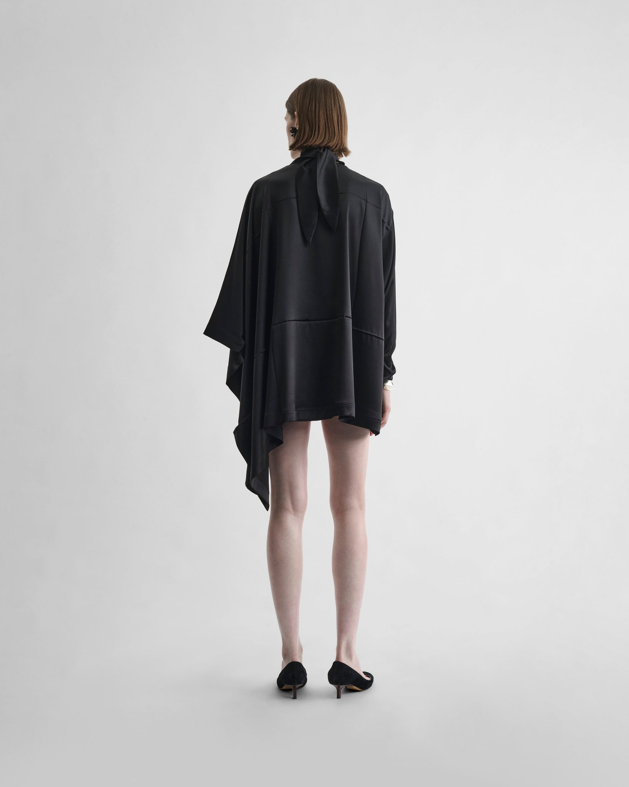 Back view of model wearing CAPED TOP in black silk