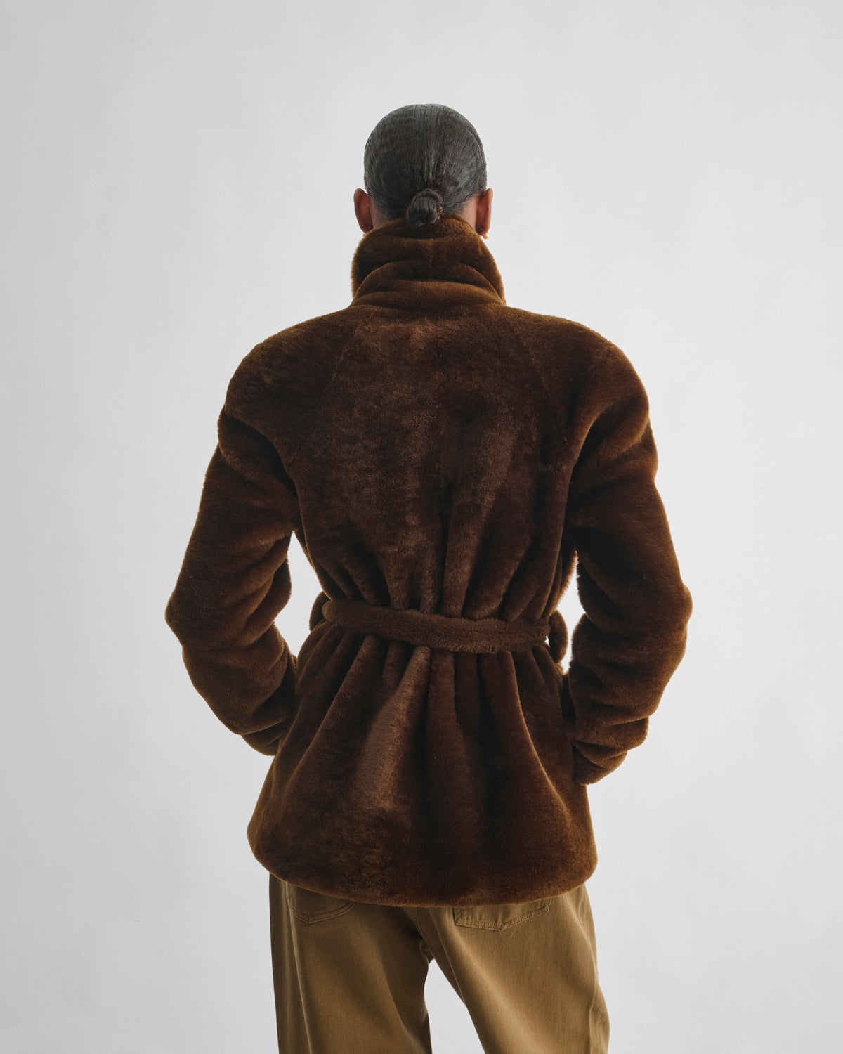 Back view of model wearing BELTED ROBE JACKET in burnt orange shearling